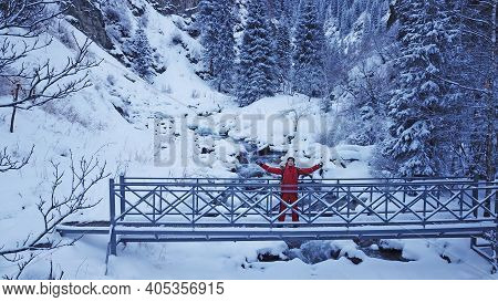 The Guy Is Walking On The Bridge Over The River. The View From The Drone To The Tall Trees, The Rive