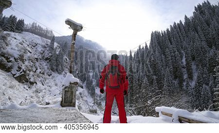 The Guy Stands On The Edge Of The Hill And Enjoys The View. Looks At A Snowy Gorge With High Mountai