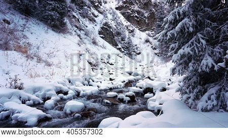 A Clear Mountain River Runs Through A Snowy Gorge. There Is A Metal Bridge Covered With Snow. Tall S