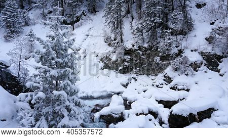 A Clear Mountain River Runs Through A Snowy Gorge. There Is A Metal Bridge Covered With Snow. Tall S