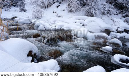 A Clear Mountain River Runs Through A Snowy Gorge. There Is A Metal Bridge Covered With Snow. Tall S