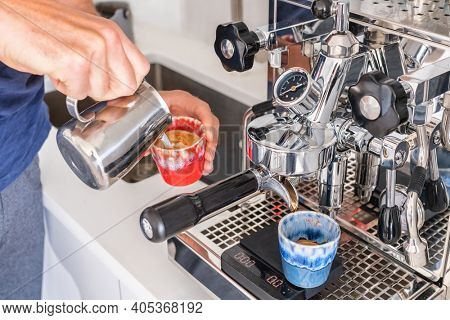 Barista man making cortado at coffee machine pouring milk in espresso cup at cafe. Home morning drink breakfast in kitchen.