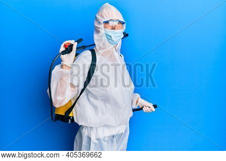 Covid specialist wearing decontamination protective suit and disinfectant spray, decontaminate and sanitize surface, standing over blue background