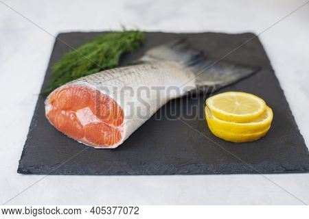 Fresh Raw Salmon Tail Fillet Part With Lemon And Dill Served On A Black Stone Board On Light Backgro