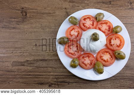 The Meal On A White Plate And Wooden Table Consists Of Sliced Tomatoes, Pitted Olives And Mozzarella