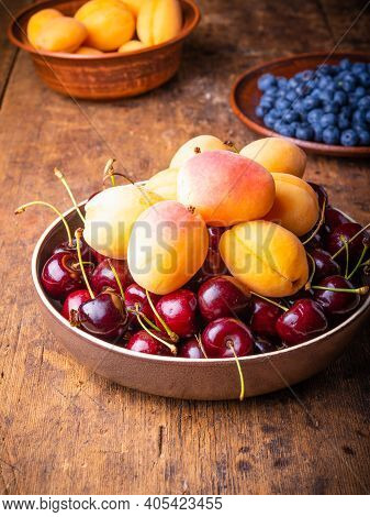 Bowl With Berries Cherries And Apricots On An Old Wooden Rustic Table Close-up Against A Background 