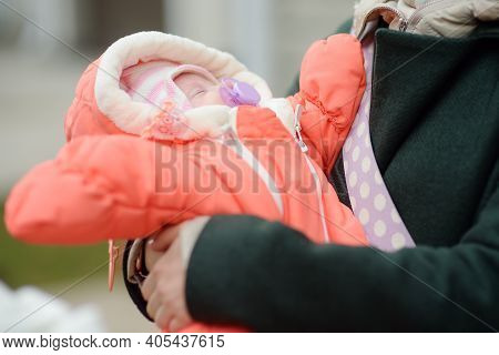 Newborn Baby Girl In Her Mother Arms. Baby Sleep Quietly And Sucks A Pacifier Warm Clothes For The B