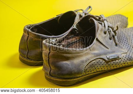 Old Torn Yellow Summer Shoes On A Yellow Background. A Pair Of Men's Heavily Worn Leather Shoes.