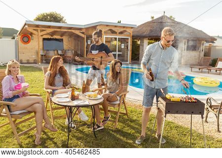 Group Of Cheerful Young Friends Having Fun Playing The Guitar And Singing At Backyard Barbecue Party