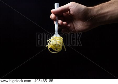Spaghetti On A Black Background. Boiled Spaghetti On A Fork. Isolated Spaghetti. Male Hand Holding A