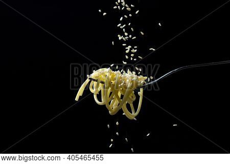 Spaghetti On A Black Background. Boiled Spaghetti On A Fork. Isolated Spaghetti. Sesame Seeds Are Po