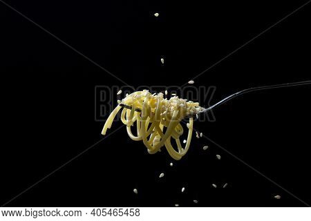 Spaghetti On A Black Background. Boiled Spaghetti On A Fork. Isolated Spaghetti. Sesame Seeds Are Po