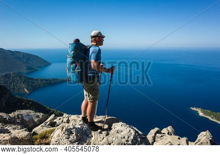 Hiking on Lycian way. Man with backpack standing on rock cliff high above Mediterranean sea enjoying the view, Trekking in Turkey on Lycian Way trail, outdoor activity