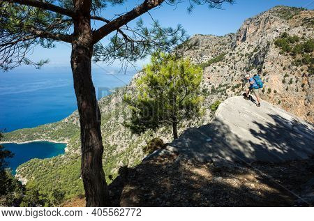 Hiking on Lycian way. Man with backpack looking down from steep rock high above Mediterranean sea, Trekking in Turkey on Lycian Way trail, outdoor activity.