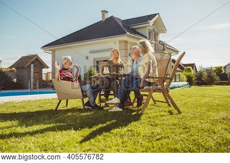 Group Of Cheerful Senior Friends Having Lunch In The Backyard By The Swimming Pool, Gathered Around 