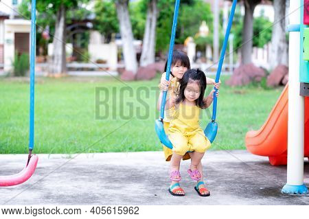 Two Cute Asian Little Sisters Playing Blue Swinging. The Eldest Sister Swings The Player For Her Sis