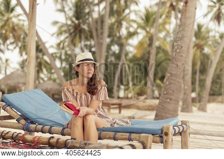 Young Woman Sitting On Sun Bed Underneath Palm Trees At Beautiful Tropical Island Exotic Beach Resor