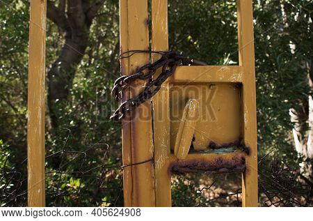 Rusty Old Iron Chain At A Fence Holding A Yellow Gate Shut
