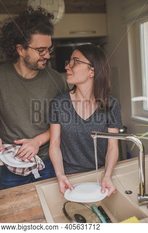 Beautiful Young Couple In Love Doing The Washing Up Together After Lunch; Woman Washing The Dishes W