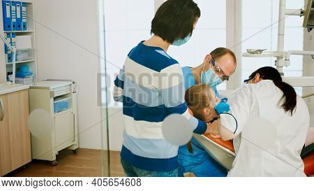 Dentistry Doctors Cleaning Teeth Of Child, Treating Dental Problems While Mother Standing Near Stoma