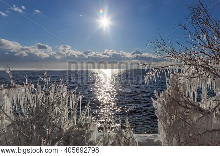 Icicles On Brunches Of Trees On The Coast Of Baikal Lake With Sun And Clouds