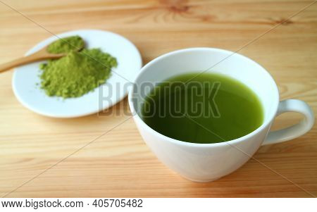 Closeup A Cup Of Hot Matcha Green Tea On Wooden Table With Blurry Matcha Tea Powder In Background