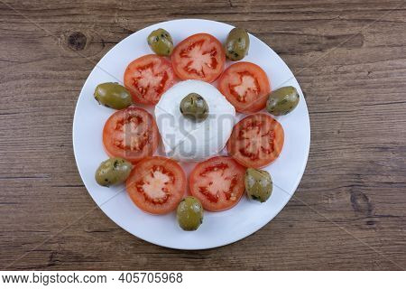 The Meal On A White Plate And Wooden Table Consists Of Sliced Tomatoes, Pitted Olives And Mozzarella
