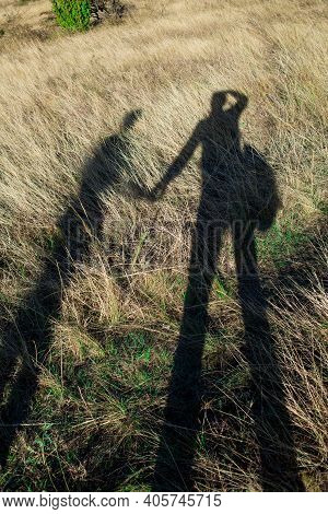 Concept Is Man And Nature. Shadow Of A Man And A Woman On The Yellowed Grass In Autumn.
