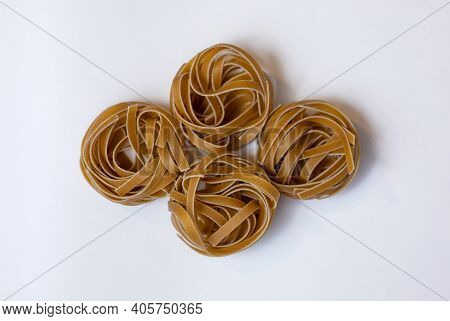 Raw Whole Grain Brown Pasta Tagliatelle On A White Background, Made With Wheat Flour, Rich In Nutrie