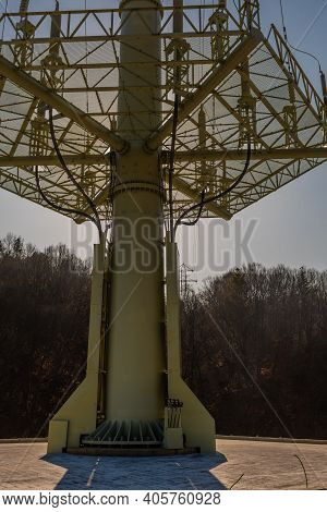 Low Angle View Of Grid Support Of Large Electrical Tower With Sun Shining From Behind Tower.