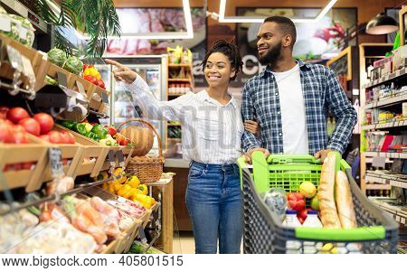 Black Family On Grocery Shopping In Supermarket. Happy African Couple Buying Organic Vegetabels And 