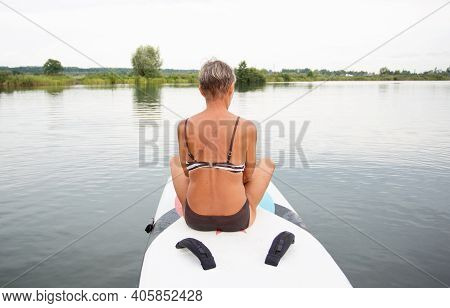 Active Senior Woman In Swim Suit Sitting On Surf In The Water