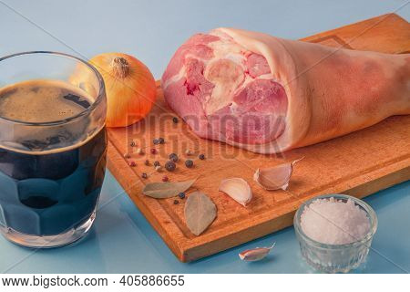 Raw Pork Knuckle, Garlic, Onion, Dried Bay Leaves, Sea Salt And Peppercorns On Wooden Cutting Board.