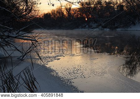 River winter landscape. Frost on ice. Fog over a non-freezing river at sunset.