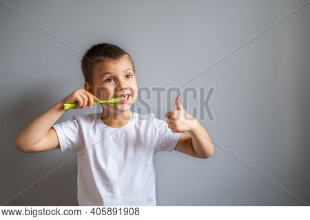 Boy Without Milk Upper Tooth In White T-shirt Holds Toothbrush In Hand On The Gray Background.