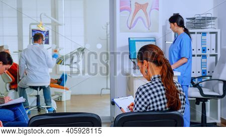 Back View Of Woman Filling In Dental Document Sitting On Chiar In Waiting Room Preparing For Teeth E