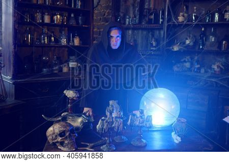 Male exorcist in hood near the magic crystal ball