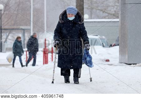 Moscow, Russia - February 2021: Elderly Woman In Medical Mask Walking With A Canes And Bag On A City
