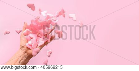Womans Hand Throws Up Pink Satin Hearts On Pink. Concept Love. Woman Gives Her Love To Whole World.
