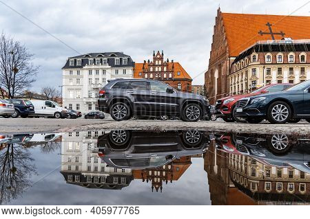Wroclaw, Poland - March 1 2020 Cars On Car Parking And Buildings Reflected In Small Puddle