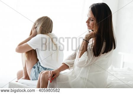 Family conflict and relations concept. Mother and daughter having quarrel and aguring at home. Sad woman and teenage girl sitting on bed. Not looking at each other.