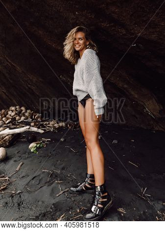 Attractive Cheerful Woman In Sweater Posing At Black Sand Beach In Bali