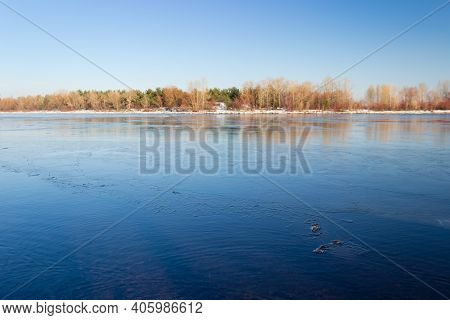 Section Of Wide Plain River Partially Covered With Thin Ice Against The Clear Sky And Forest On An O