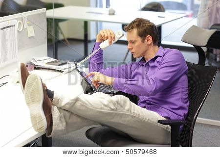 Young businessman caucasian in his office on phone working with tablet - bad sitting posture 