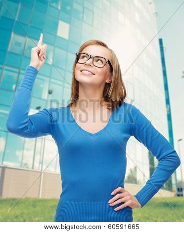 advertisement concept - attractive young woman in casual clothes and black eyeglasses pointing her finger up