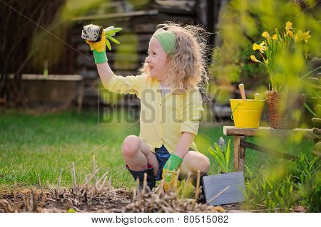 adorable happy child girl plays little gardener and planting flowers in spring garden