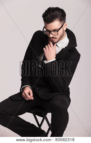 Elegant business man holding his hand to his chin, thinking while sitting on a stool.