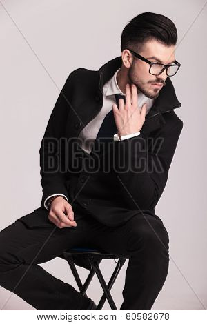 Handsome elegant business man sitting on a stool while looking down and holding two fingers to his chin.