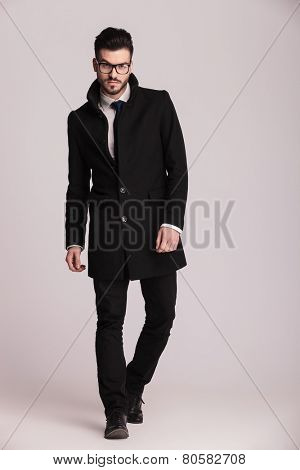 Handsome young business man wearing a long black coat walking towards the camera.