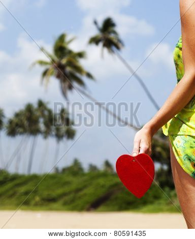 Woman holding red heart on exotic sandy beach - Love concept